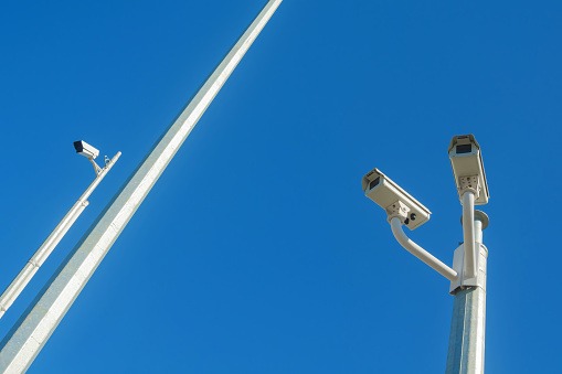 Looking up at three CCTV security cameras atop a pole against a clear sky