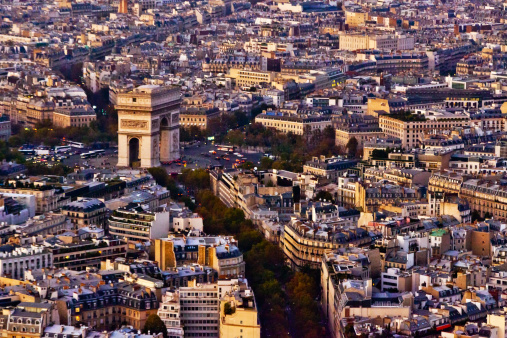 The Arc of Triumph (Arc de Triomphe) presides over downtown Paris, France in the soft light of dusk. This image was captured from a high level in the Eiffel Tower.