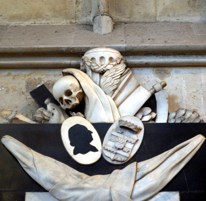 Memento mori (Remember thou shalt die) - Ancient medieval sculpture with skull and reaper's sickle in Koelner Dom cathedral, Koeln, Germany