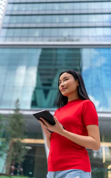 istock Young asian woman using her digital tablet casually in a central business district against the backdrop of corporate buildings. Connected Mobility. 1757276455