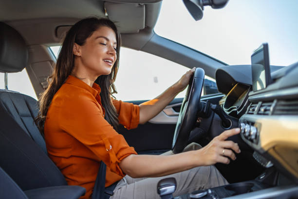 mujer de negocios feliz escuchando música mientras viaja con su automóvil por la ciudad. mujer encendiendo el sistema de aire acondicionado del coche, botón de encendido y apagado del aire acondicionado del coche - car dashboard air conditioner driving fotografías e imágenes de stock