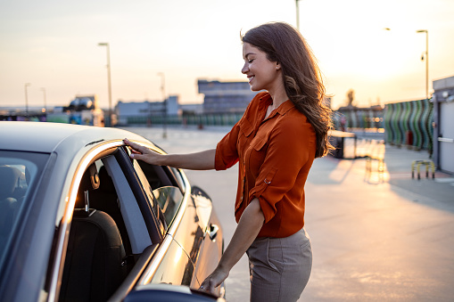 Successful woman standing outside and opening the car door. Businesswoman getting into the car