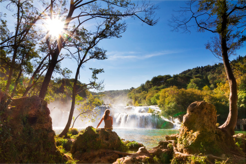 Beautiful woman sits at the waterfall in Krka national park, Croatia