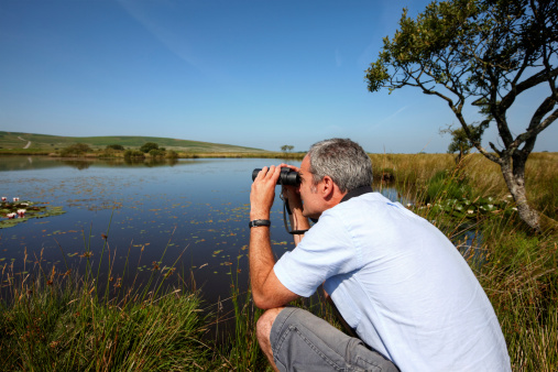 Mature caucasian man  through binoculars at lily pond