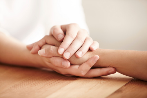 Hands holding one another on a table in prayer