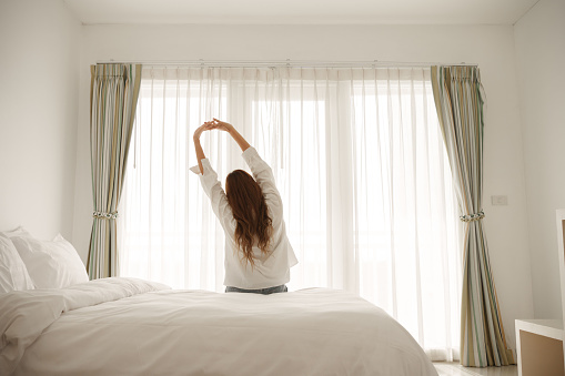 Young asian woman sitting on the bed and stretch oneself in the morning at home.