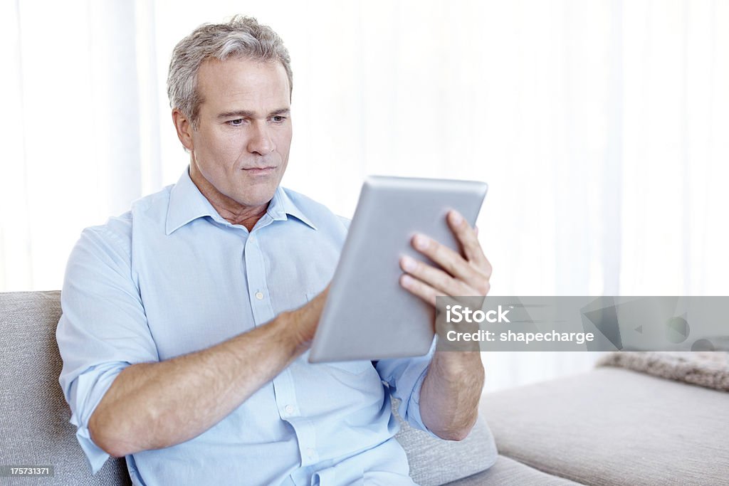 Trying to navigate its many functions Mature man sitting on the sofa and using a digital tablet 50-54 Years Stock Photo