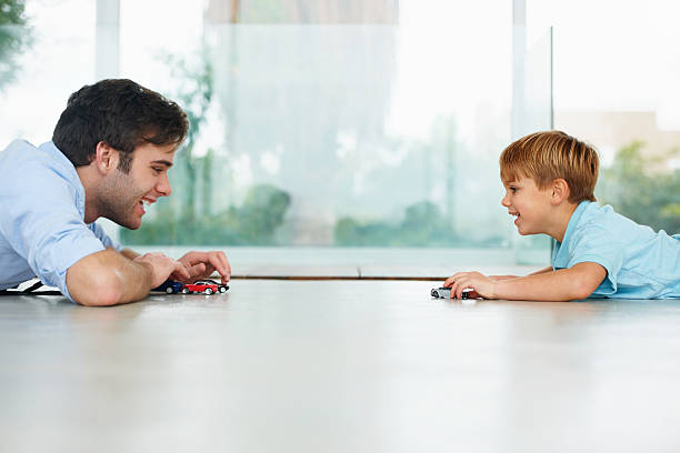 Enjoying some father-son time A cute boy and his young father playing with toy cars on the floor kid toy car stock pictures, royalty-free photos & images
