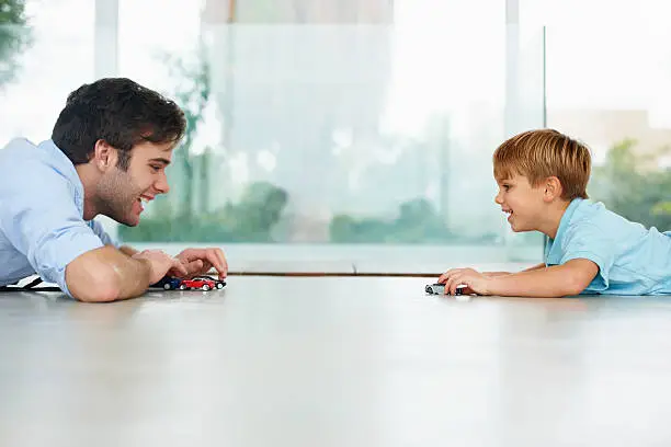 A cute boy and his young father playing with toy cars on the floor