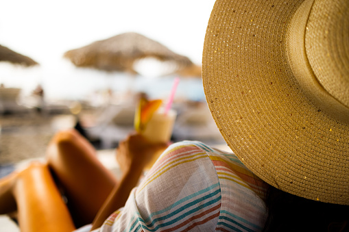 Close up of a woman with sun hat spending her summer day relaxing on a deck chair at the beach.