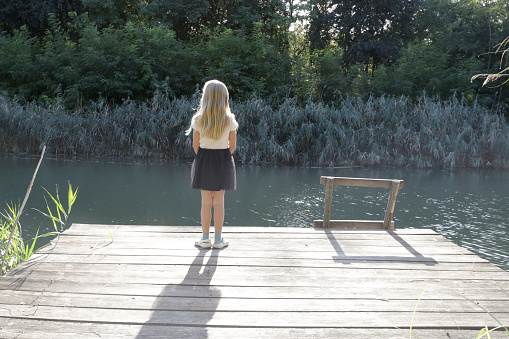 Rear view of little blond girl on a dock overlooking at water