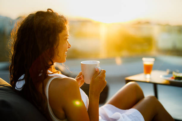 donna felice che si gode un caffè su un patio al tramonto. - balcony women patio coffee foto e immagini stock