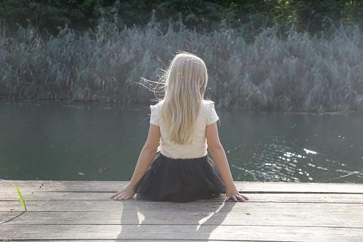 Rear view of little blond girl on a dock overlooking at water
