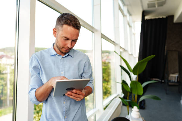 istock Modern businessman using digital tablet while standing near window in his office 1757339172