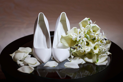 Beautiful white women's shoes. There is a bouquet and rose petals nearby. Shoes for weddings or special events.