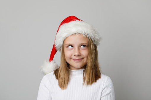 Cute mischievous child girl in Santa hat looking up on white background