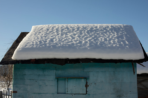 Plank shed. The village in winter. Wooden building. Snow on the roof of the house.