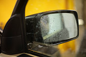 Rearview mirror in water droplets. Car wash in the garage. Wet machine.
