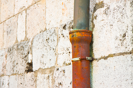 Old cast iron and copper downpipe against a stone wall - (Italy) - image with copy space