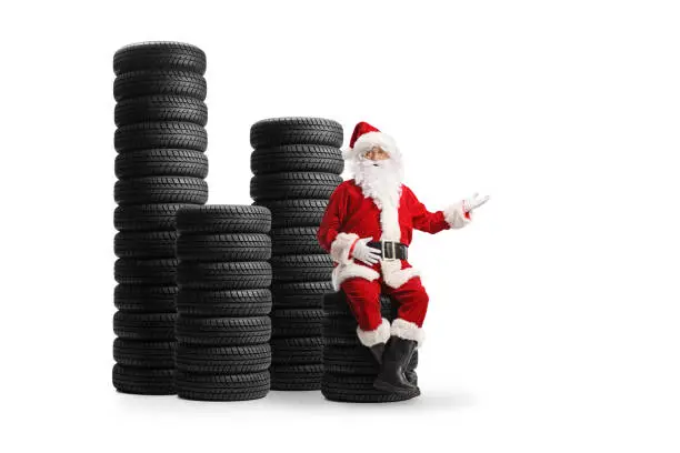 Santa claus seated on top of a pile of tires and gesturing a welcome sign isolated on white background