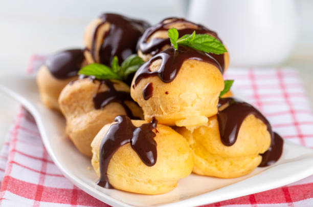 istock Delicious profiteroles with chocolate and white plate. Selective focus image on light background. 1757411937