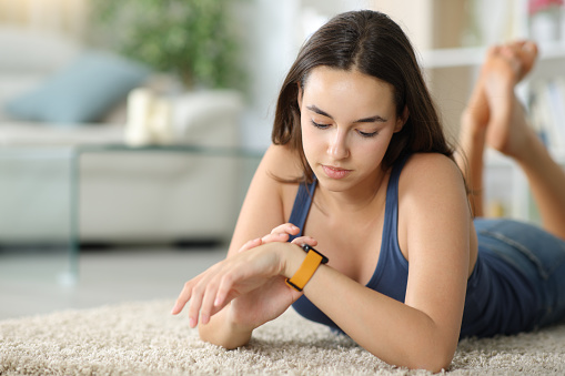 Woman checking smartwatch on the floor at home