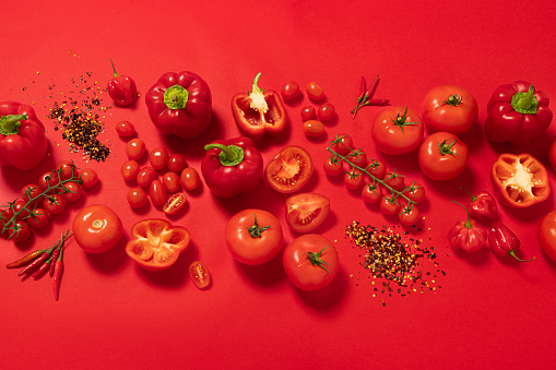 Top view of a large group of red vegetables such as various kinds of tomatoes and peppers arranged on a banner shape on red background