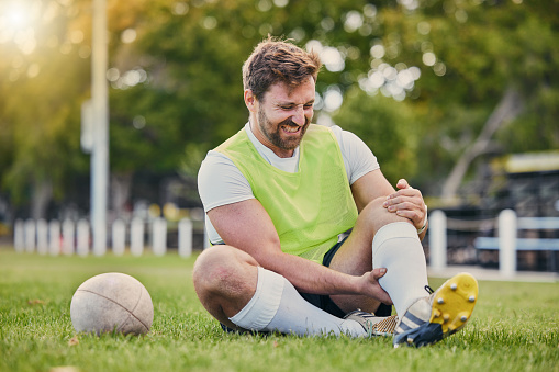 Football, man and knee pain on grass field, inflammation and bruise with training, workout and exercise. Male player, athlete or guy on ground, leg injury and health issue with practice and emergency