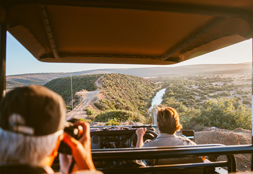 Safari vehicle with passengers driving along a dusty road running through bush land in a national park