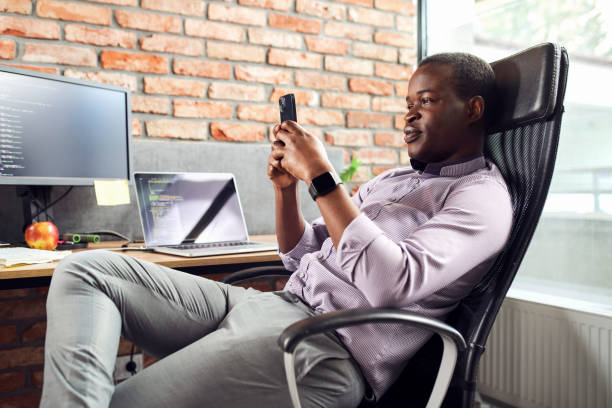Young adult man mobile app developer sitting relaxed at office using phone stock photo