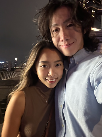 Asian Chinese couple selfie with smart phone in Tsim Sha Tsui promenade, Kowloon, Hong Kong at night