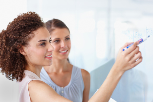 Two businesswomen working on a whiteboard together