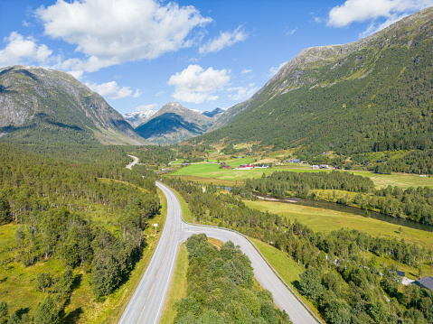 Aerial view of a road surrounded by green landscape, mountains. Sunny day
