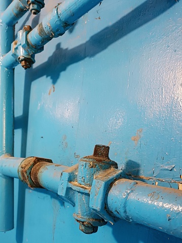 Very old dirty blue Pipe construction. Vertical and horizontal pipes with connecting elements. Blue gas pipes, connecting element at blue wall. Gas equipment Part. Free focus. Indoor Gas Line.