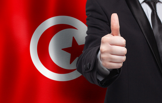 Tunisian concept. Businessman showing thumb up on the background of flag of Tunisia