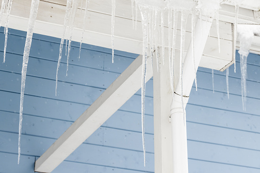 Icicles hang on the rural house roof over blue wall background