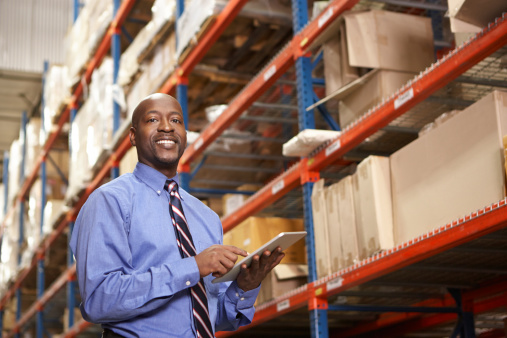 Businessman With Digital Tablet In Warehouse Looking At Camera Smiling