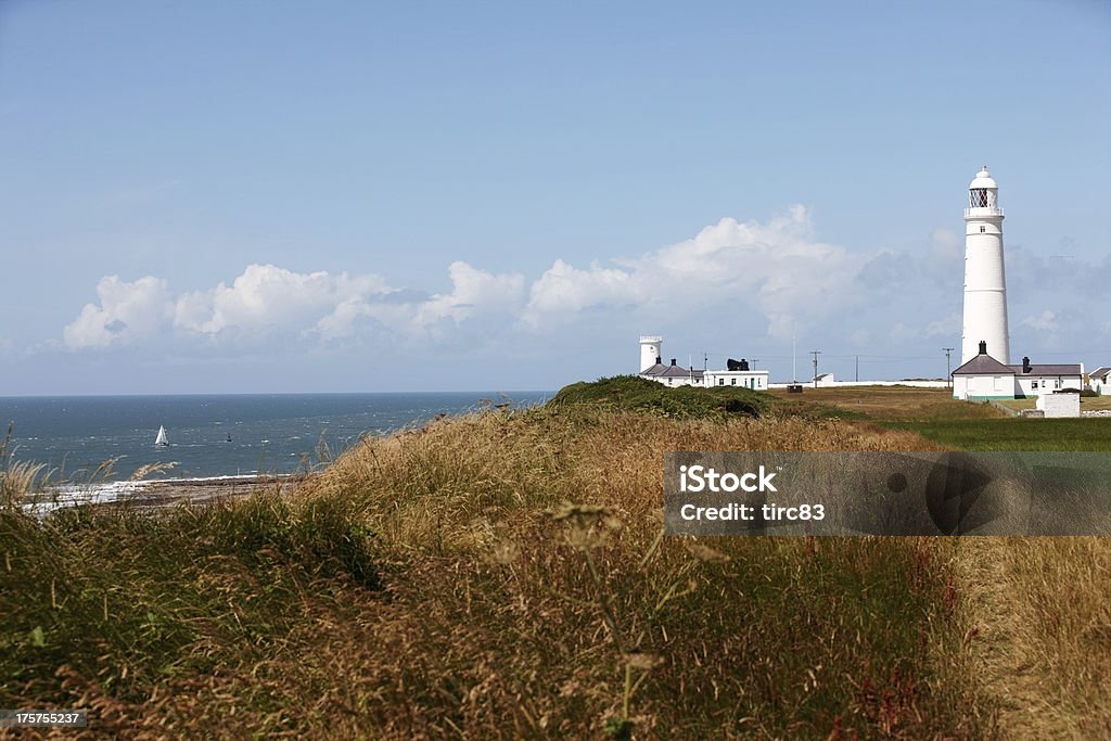 White lighthouse against blue sky and sailing boat on sea White lighthouse against blue sky and sailing boat on sea at Nash Point on the south coast of Wales Agricultural Field Stock Photo