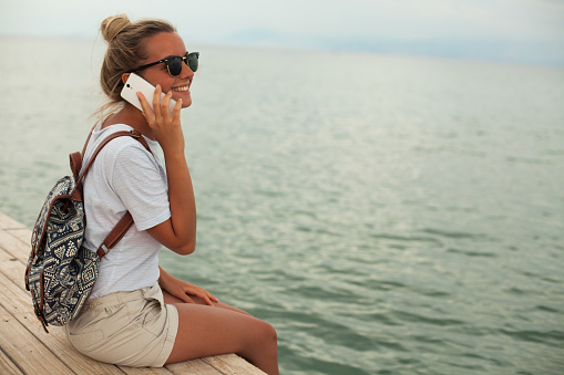 Smiling woman on beach talking with smartphone