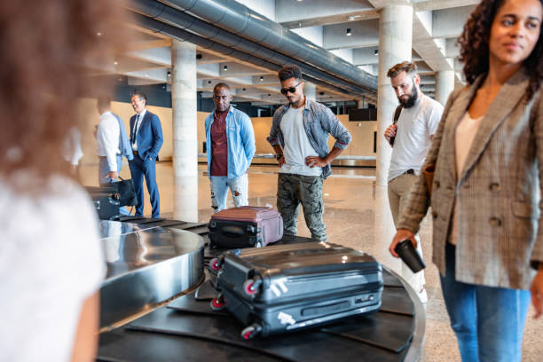 Multicultural People Waiting For Their Belongings At The Baggage Band Three-quarter side shot with blurred background of a multicultural group of people of different ages waiting for their belongings at the baggage band, in the arrivals zone of the airport. walking into glass door stock pictures, royalty-free photos & images