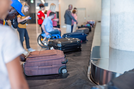 Three-quarter side shot with blurred background of a multicultural group of people of different ages waiting for their belongings at the baggage band, in the arrivals zone of the airport.