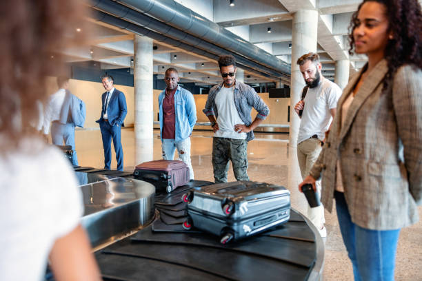 Multicultural People Waiting For Their Belongings At The Baggage Band Three-quarter side shot with blurred background of a multicultural group of people of different ages waiting for their belongings at the baggage band, in the arrivals zone of the airport. walking into glass door stock pictures, royalty-free photos & images