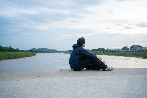 asian man sit and relax at side of river during sunset