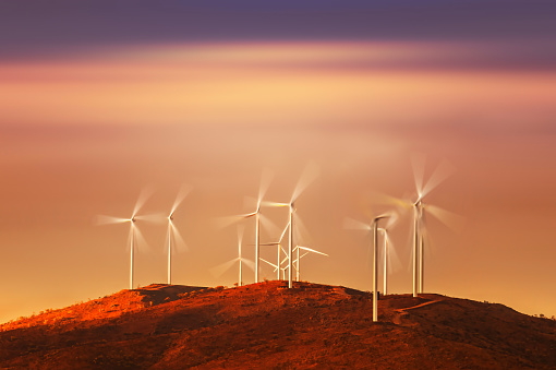 Wind turbine farm in motion on hill at sunset in desert in outback Australia