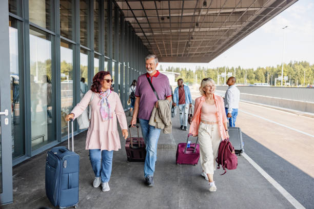 Multiple Multicultural Passengers Getting Ready To Enter The Airport Full length front shot with blurred background of multiple multicultural passengers of different ages optimistically getting ready to enter the airport and do their check-in for their upcoming flight on a sunny day. walking into glass door stock pictures, royalty-free photos & images