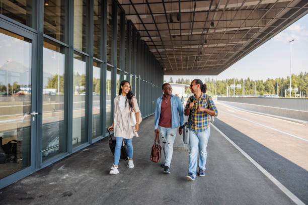 Multicultural Passengers Walking Towards The Airport Departure Door Full length front shot with blurred background of a multicultural passengers group of different ages enthusiastically walking towards the airport departure door to do their check-in for their upcoming international flight on a sunny day. walking into glass door stock pictures, royalty-free photos & images