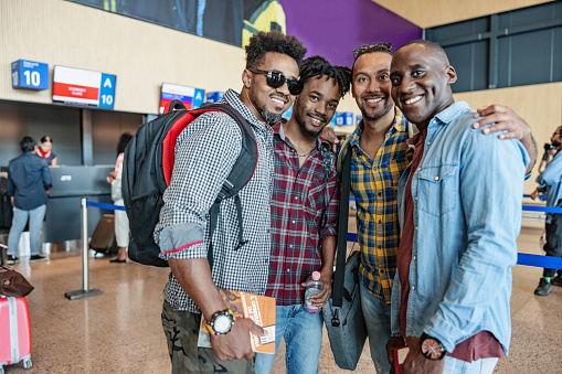 Three-quarter shot of two Latin-American and two African-American passengers smiling at the camera while holding their personal items excited to start a new adventure for the holidays.