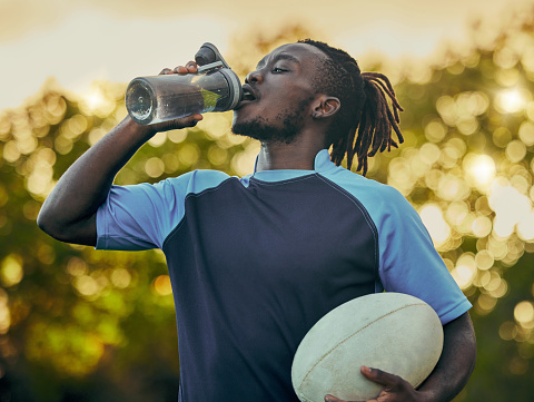 Drinking water, fitness and rugby with a sports black man outdoor for a competitive game or event. Exercise, training and health with a male athlete taking a drink from a bottle during a break