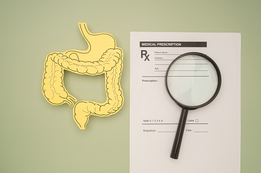 Top view of an intestine symbol made from yellow paper and a magnifying glass over the medical prescription sheet on a green background. Treatment and prevention of constipation and diarrhea