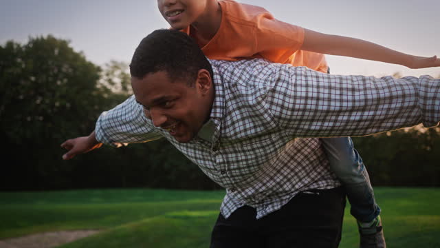 Multiracial father piggybacking cheerful son on fresh air